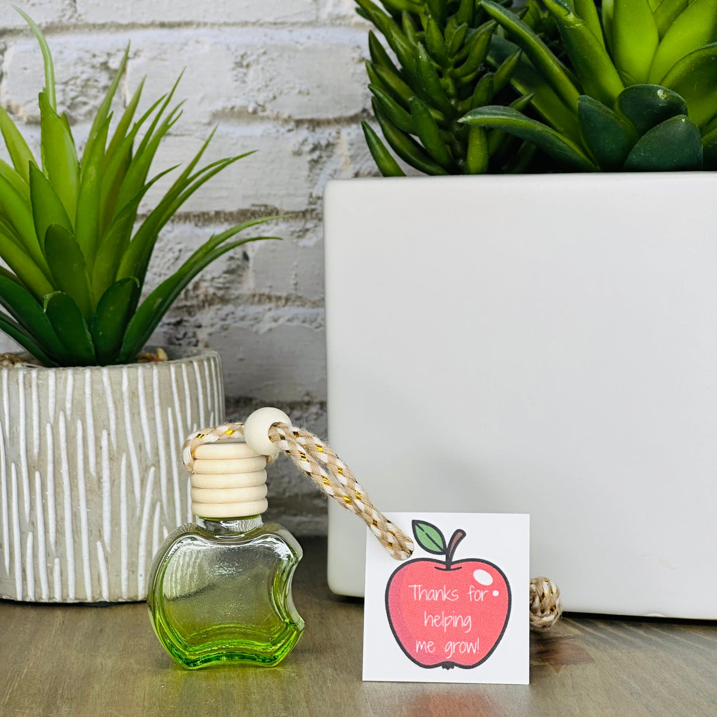 Small green bottle with a white cap, a pink apple card, and plants on a wooden surface.