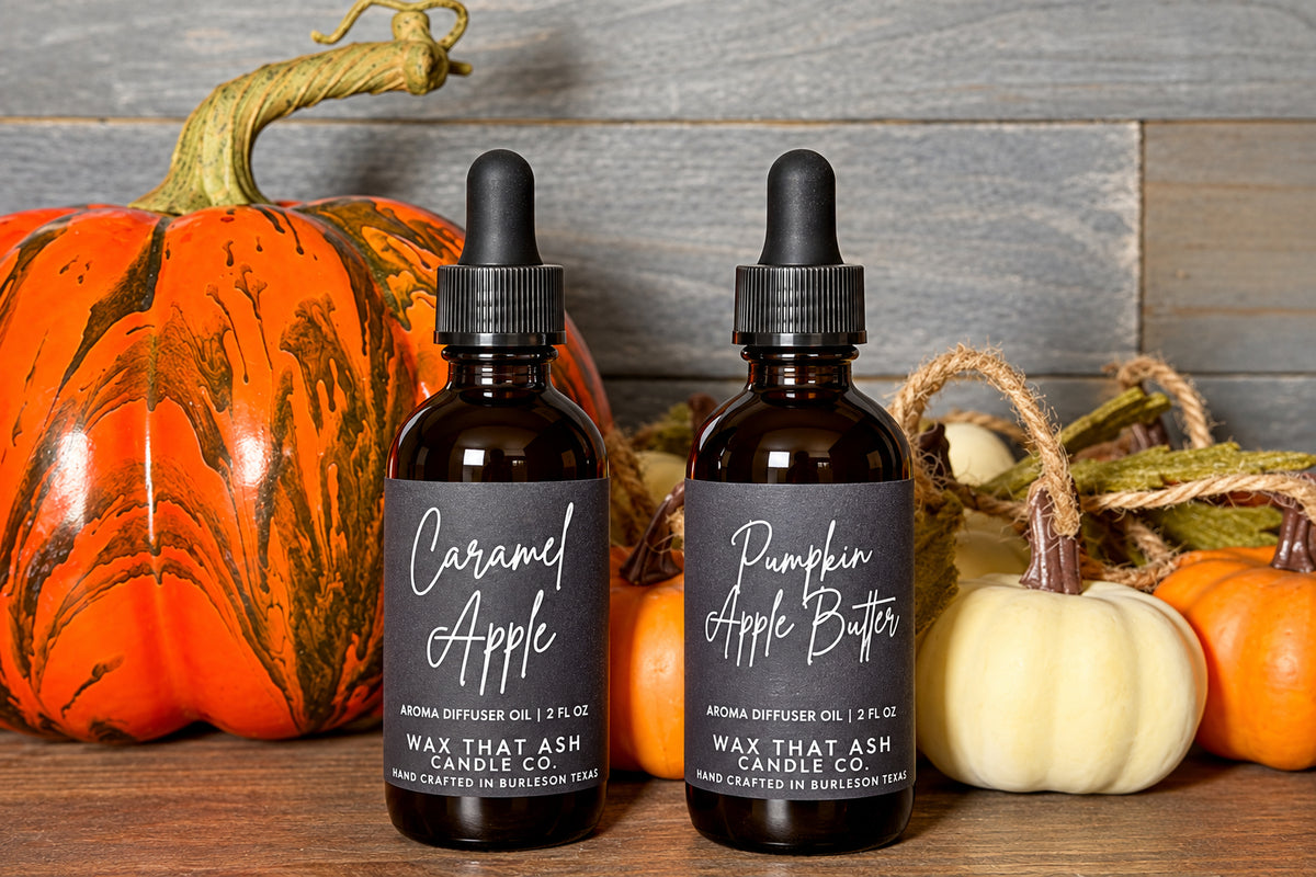 Two amber glass dropper bottles labeled 'Caramel Apple' and 'Pumpkin Apple Bites' by Max That Ash, styled on a wooden surface with decorative pumpkins against a rustic gray wood plank background.