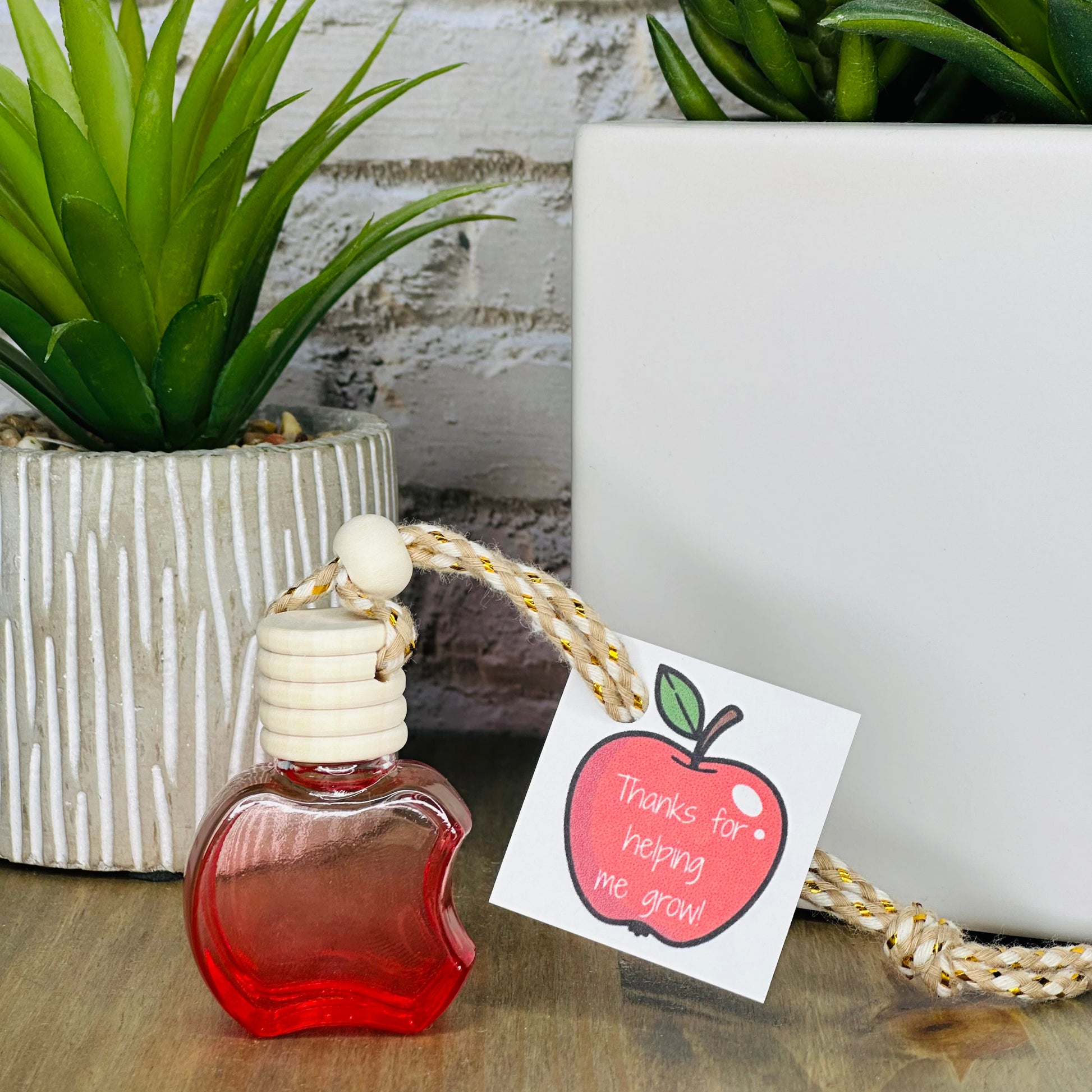 Small red bottle with a white cap on a wooden surface, next to a plant and a card with an apple illustration.